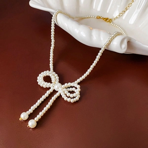 Detailed view of a white pearl necklace with a 3D woven bow pendant on a shell tray