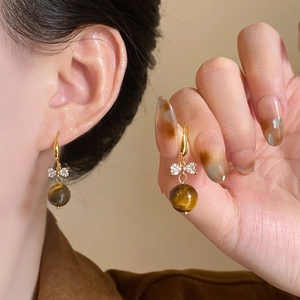Detail of tiger eye drop earring with golden bow and sparkling cubic zirconia inlay