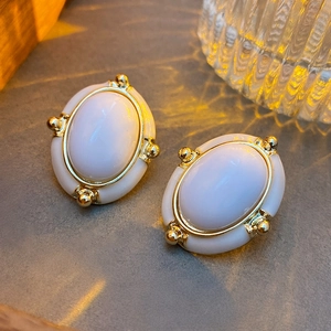 Macro shot of oval vintage earrings with white enamel and gold trim on concrete
