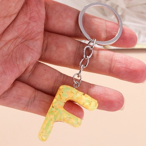Detail view of a letter F keychain filled with green and yellow sequins in hand