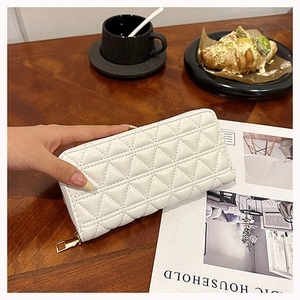 Detailed view of white quilted long wallet with golden zipper in a cozy cafe setting