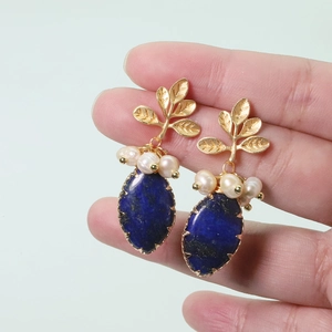 Macro detail of gold leaf earring with white pearl and deep blue gemstone inlay