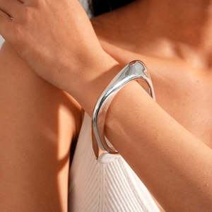 Detailed view of irregular polished silver metal bangle on wrist with liquid aesthetics