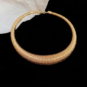 Golden chunky choker necklace with spiral metal texture and lobster clasp on black backdrop