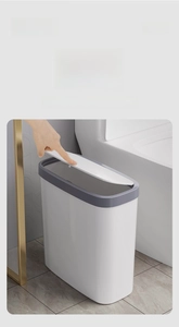 Close-up of slim white press-top trash can being opened by hand in a modern bathroom