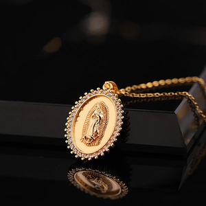 Gold Virgin Mary oval pendant necklace with white zircon stones on a reflective surface