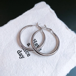 Macro shot of silver minimalist C-shaped hoop earrings on textured white paper card