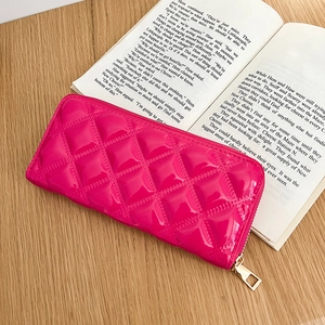 Detail of fuchsia quilted patent leather clutch purse with gold zipper on a wooden desk