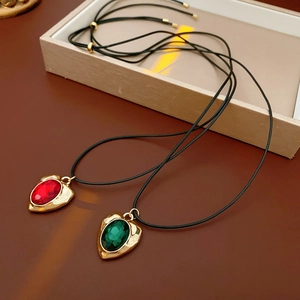 Detail of vintage gold heart pendants with red and green gems on black cord necklaces