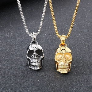 Detailed view of silver and gold skull pendants on round box chains in a dark rock style