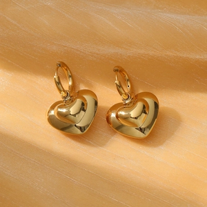 Close-up of golden heart earrings on textured fabric showing high mirror finish details