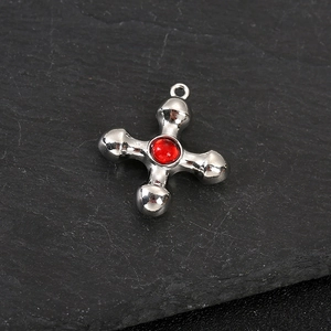 Detail of silver cross pendant with red gemstone on textured slate background
