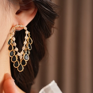 Close-up of gold tassel earrings featuring black teardrop gems and sparkling cubic zirconia