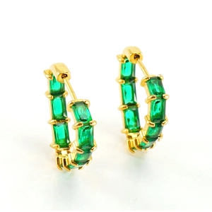 Macro shot of gold huggie earrings featuring emerald-cut green cubic zirconia stones