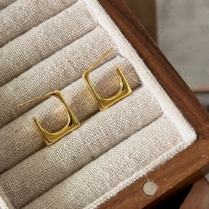 Macro shot of gold square geometric earrings displayed on a linen jewelry box tray