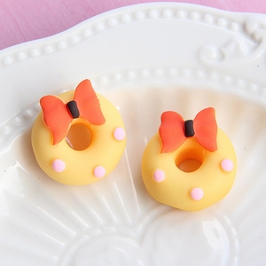 Macro view of a yellow resin donut with a red bow and pink dots on a white plate