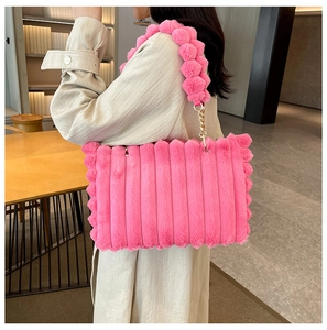 Pink plush tote bag featuring textured vertical stripes and decorative fur ball chain strap