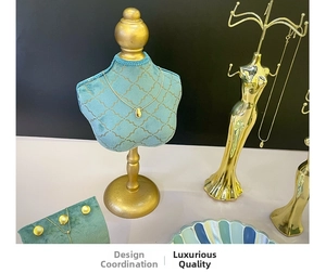 Detail of gold teardrop necklace and stud earrings on green velvet bust display