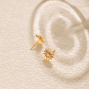 Macro shot of gold sunflower stud earrings with sparkling center zircon and elegant shadows