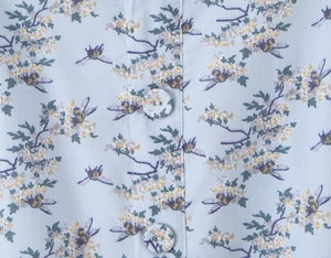 Macro view of light blue floral fabric with matching covered buttons and bee print