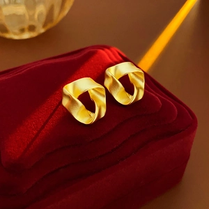 Close-up of golden geometric twisted earrings with a matte brushed metal finish texture