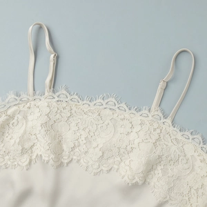 Dettaglio dello scollo in pizzo a ciglia e del tessuto satinato sull'abito bianco