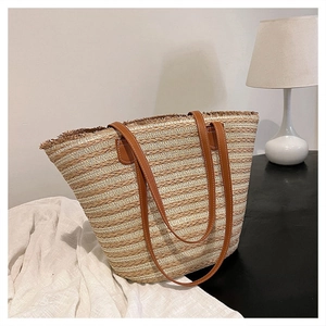 Detail of woven straw tote bag featuring brown leather handles and fringe tassels