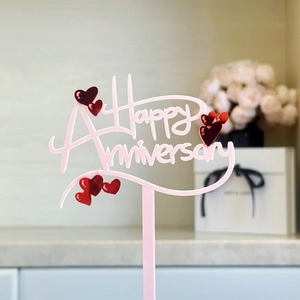 Pink acrylic Happy Anniversary cake topper with red heart decor on romantic background