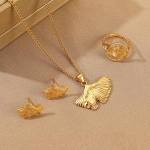 Golden ginkgo leaf jewelry set including necklace, earrings and ring on beige fabric
