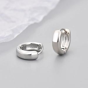 Close-up of polished silver huggie earrings on a minimalist grey background