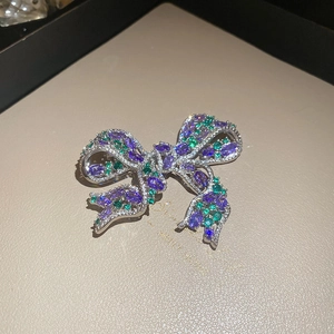 Macro shot of vintage silver bow brooch with vibrant purple and green gemstone pavé