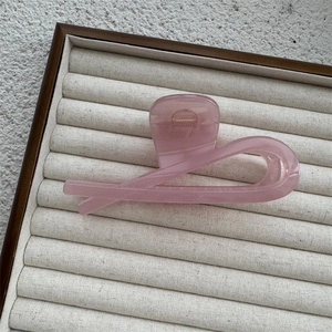 Close-up of a translucent pink hair claw clip in a minimalist twisted design