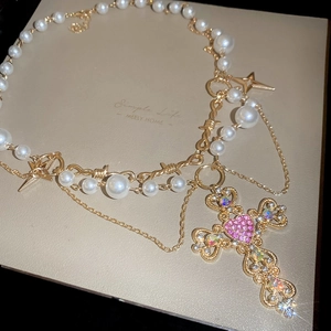 Detail view of pearl necklace featuring a pink heart rhinestone cross pendant