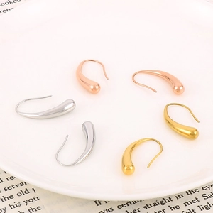 Three colors of teardrop stainless steel earrings displayed on a white ceramic plate