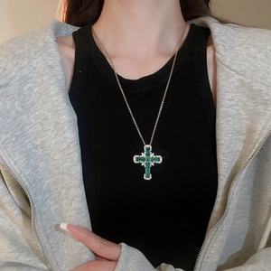 Gros plan d'un collier croix doré avec des pierres vert émeraude sur un mannequin
