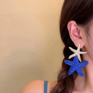 Detail view of oversized blue straw-woven and gold starfish earrings worn on model ear