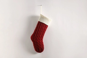 Detail of red cable-knit Christmas stocking with white ribbed cuff hanging on white wall
