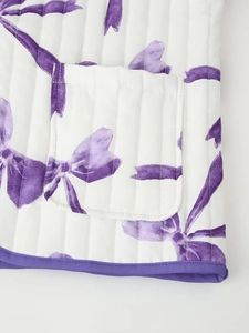 Detail of white quilted jacket with purple bow patterns, featuring pocket and purple piping
