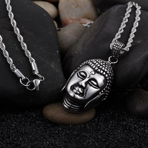Detail of silver Buddha head pendant with rope chain on natural black pebbles