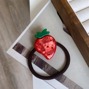 Close-up of strawberry hair tie with red rhinestones and green leaves on elastic band