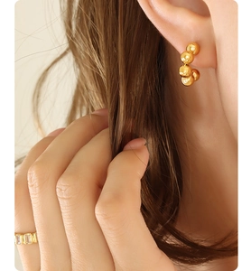 Detail of gold C-shaped earring with connected metal spheres and matching gold ring