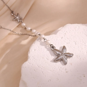 Detail of silver starfish necklace with white pearls on a textured stone and silk background