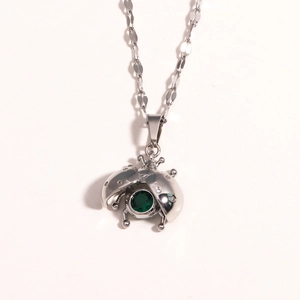 Detail of silver titanium ladybug pendant with green gemstone and diamond accents