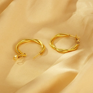 Macro shot of twisted gold hoop earrings on luxury champagne silk fabric background