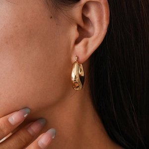 Macro shot of chunky gold teardrop earrings with a polished mirror finish on model