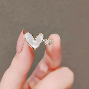 Dettaglio anello dorato con cuore bianco e diamanti pavé indossato al dito