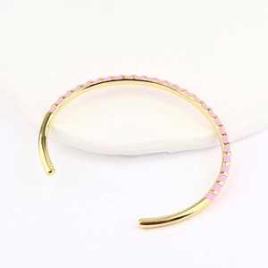 Detail of gold open bangle with pink enamel stripes on a white display stand