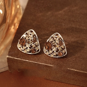 Macro shot of silver triangle earrings with inlaid brown and amber crystals on wood