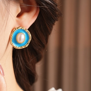 Close-up of vintage gold rimmed earrings with blue enamel and central pearl on model