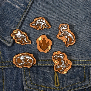 Detail of dinosaur fossil enamel pins pinned to a blue denim jacket in a radial arrangement